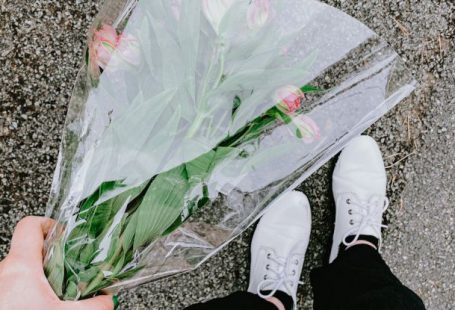 Gift - Top view of anonymous person in casual clothes and white sneakers holding bouquet of flowers and standing on asphalt