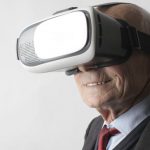 Wearable Devices - Smiling elderly gentleman wearing classy suit experiencing virtual reality while using modern headset on white background