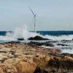 Energy-Efficient - A wind turbine on the beach with waves crashing in the background