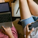 Organization Apps - From above of crop girlfriends in home clothes sitting on floor with laptop and smartphone while spending time together and planning weekend