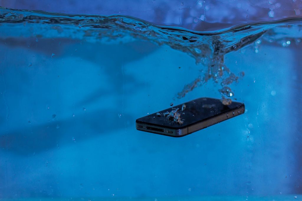 A smartphone underwater creating bubbles and movement in clear blue water.