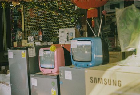 A storefront display featuring vintage televisions and home appliances on a sunny day in Bangkok.