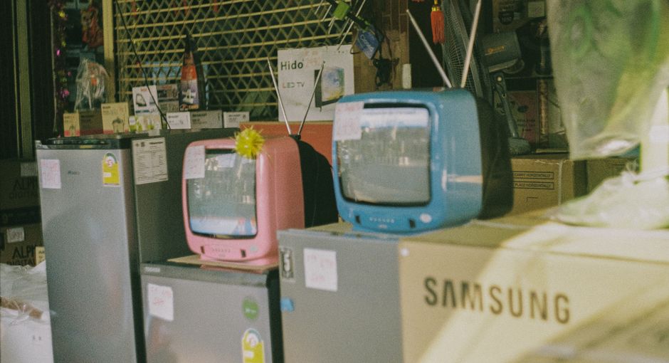 A storefront display featuring vintage televisions and home appliances on a sunny day in Bangkok.