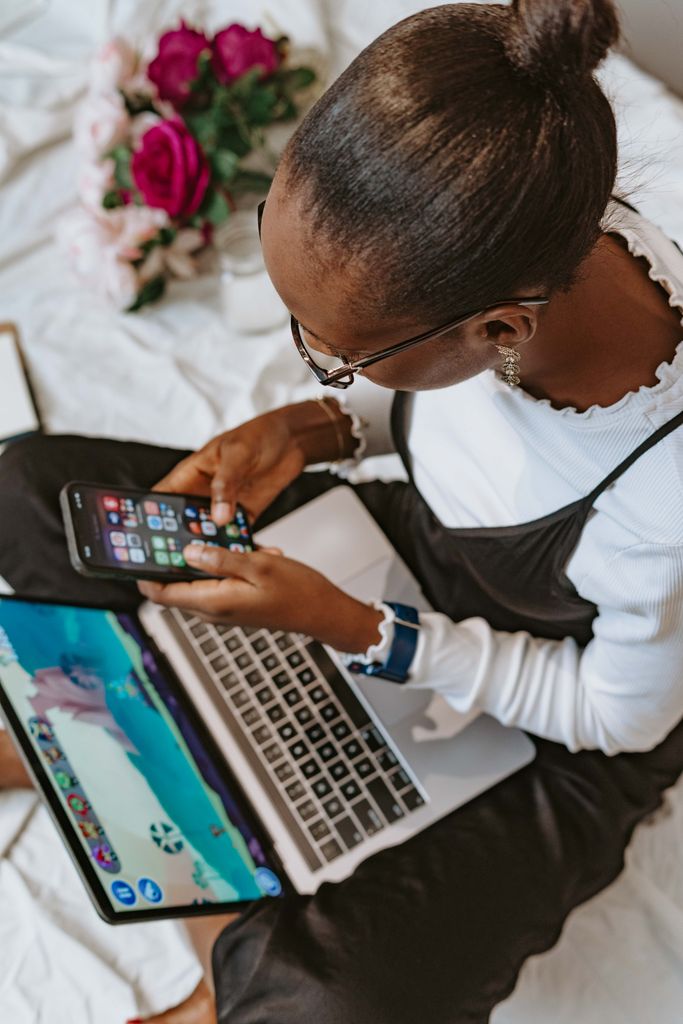 A young woman multitasks with a smartphone and laptop while seated indoors. Vibrant and modern lifestyle.