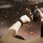 Back view of anonymous female using smartphone app and smart watch after jogging in park