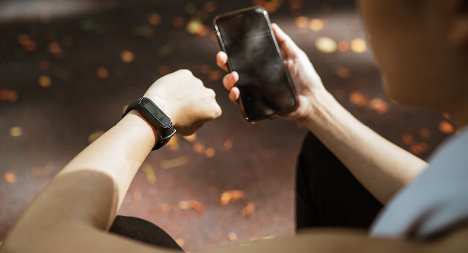 Back view of anonymous female using smartphone app and smart watch after jogging in park