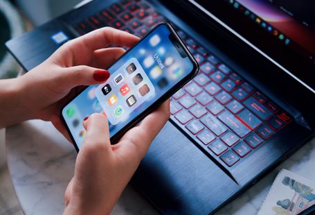 Close-up of a woman using a smartphone and laptop with red keyboard in an indoor setting.