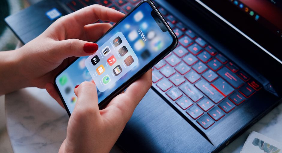 Close-up of a woman using a smartphone and laptop with red keyboard in an indoor setting.