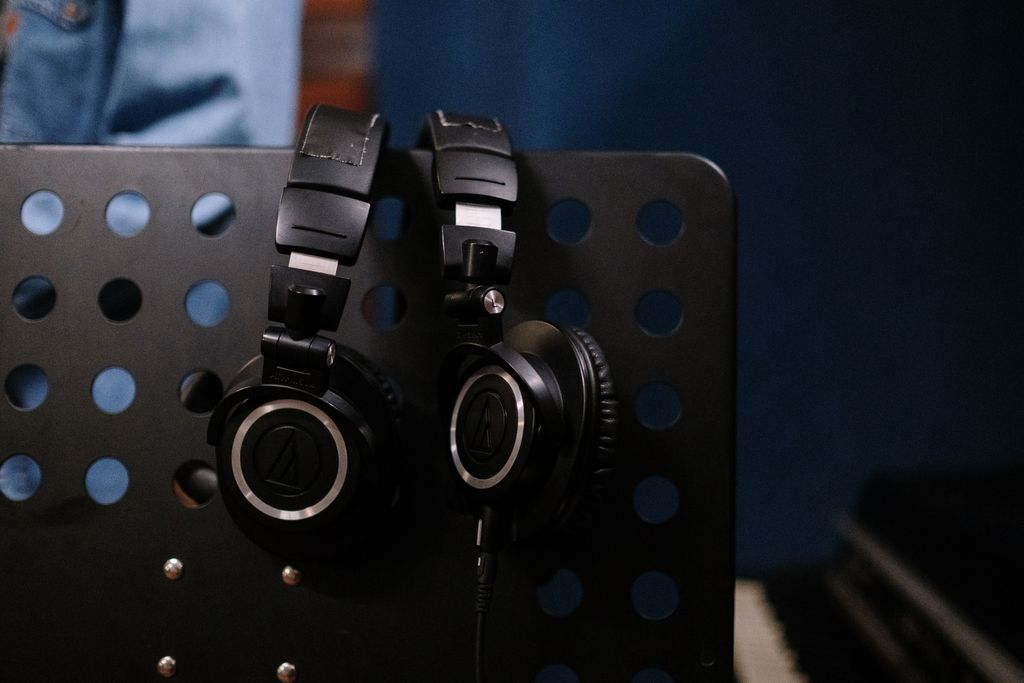Close-up of professional headphones hanging on a perforated music stand in a studio setting.
