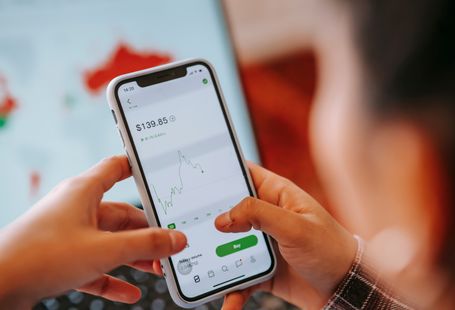 Mobile Apps Manage Finances — Crop anonymous trader using app on cellphone with graph and dollar price on screen in house