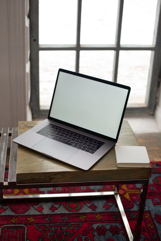 Modern workspace with a laptop and notepad on a wooden table near a large window.