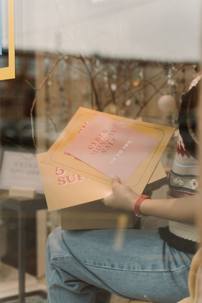 Person holding sale posters indoors, showcasing Cyber Monday and seasonal offers.