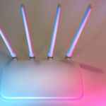 Sleek white wireless router with four antennas emitting soft blue and pink light.