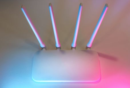 Sleek white wireless router with four antennas emitting soft blue and pink light.