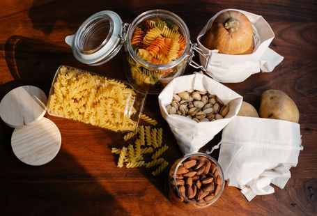 Sustainable Food Brands - Top view jars of raw pasta placed on wooden table near ECO friendly sacks with pistachios and almonds near pumpkin and potatoes
