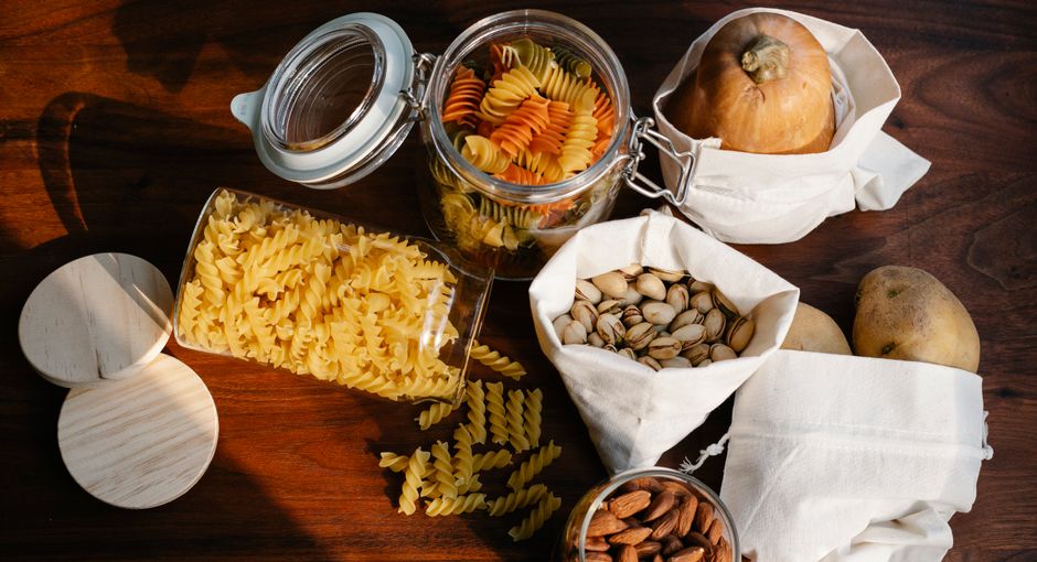 Sustainable Food Brands - Top view jars of raw pasta placed on wooden table near ECO friendly sacks with pistachios and almonds near pumpkin and potatoes