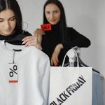Two women enjoying Black Friday shopping with discounts and deals on clothes.