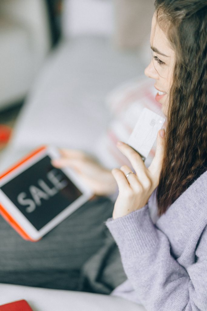 Woman holding a credit card and tablet with 'Sale' for online shopping.